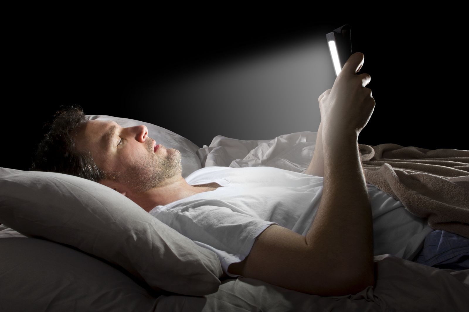 man using smartphone while laing on bed in dark